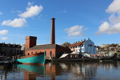 A landscape of Underfall Yard. The old hyraulic engine house and connected accumulator has been transformed into a visitor centre and popular cafe for guests to come and learn about the boatyard and enjoy a nice coffee and meal