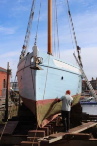 A pilot cutter vessel places on an historic slipway. This allows the worker to paint the side of the boat on a sunny day