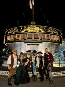 Group of pirate costumed people posing in front of the ship SS Great Britain, Bristol. The pirate band have just finished a show performing on board