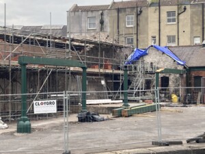 Construction site with scaffolding and a partially demolished building. The front posts has been replaced and the installation of beams across the pillars are in progress